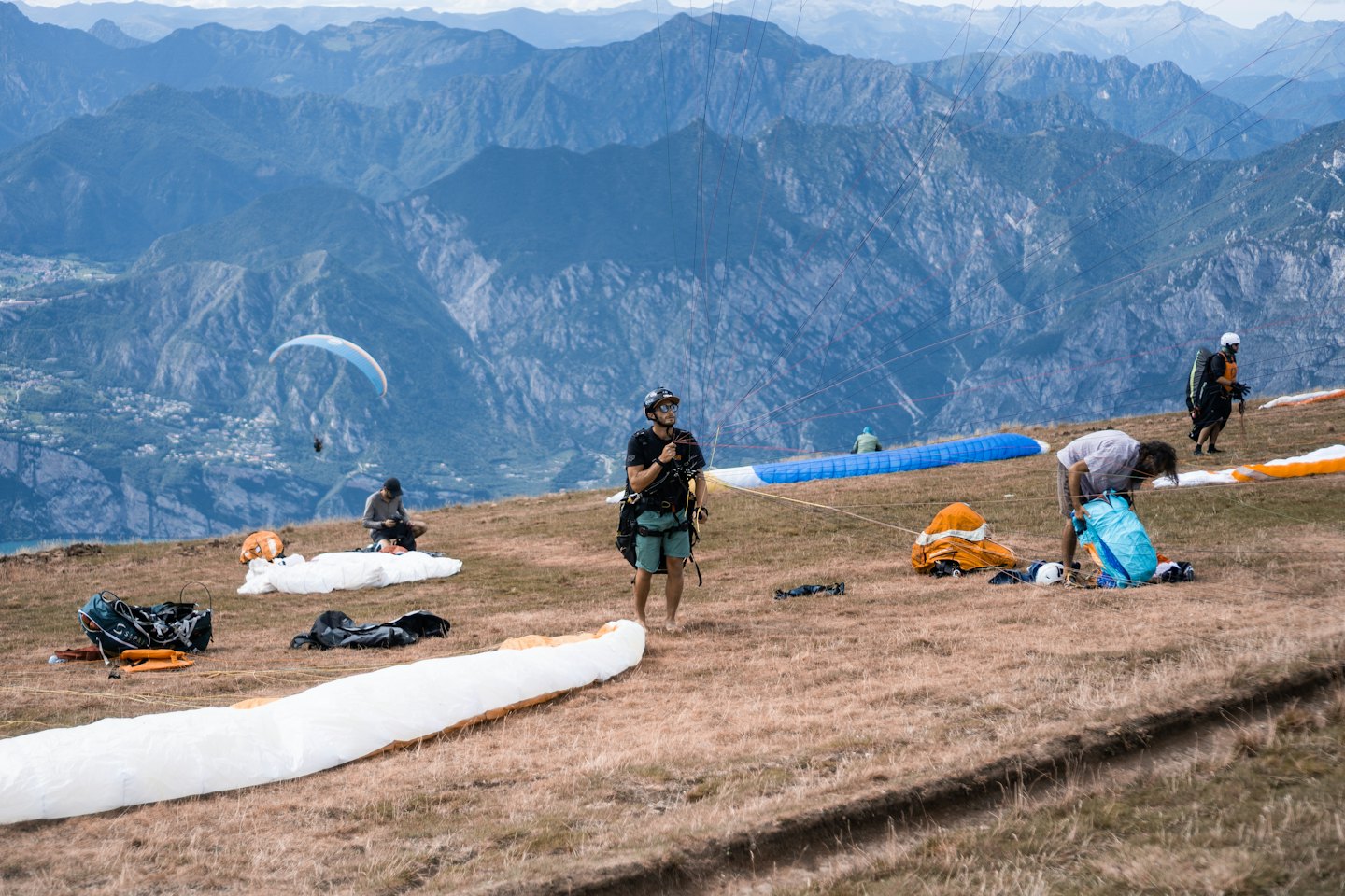 Gleitschirmflieger bereiten ihre bunte Ausrüstung auf einem grasbewachsenen Berghang vor.