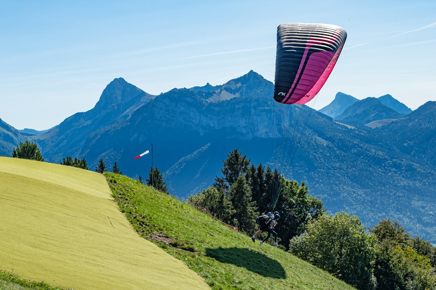 Ein Gleitschirmpilot bereitet sich auf den Start von einem grasbewachsenen Berghang vor.