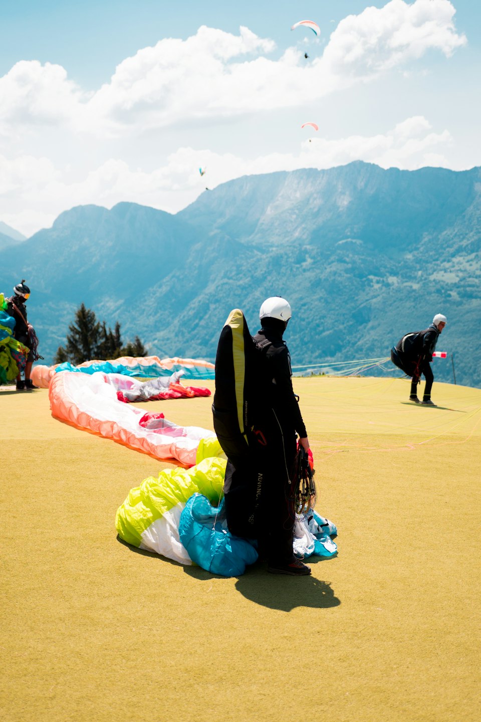 Gleitschirmflieger bereiten bunte Ausrüstung auf einem sonnigen Bergstartplatz vor.